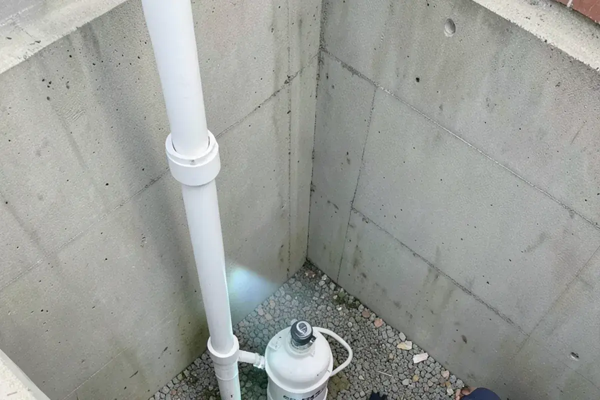 New sump pump in a basement pit in New Baltimore with a check valve and white PVC discharge pipe