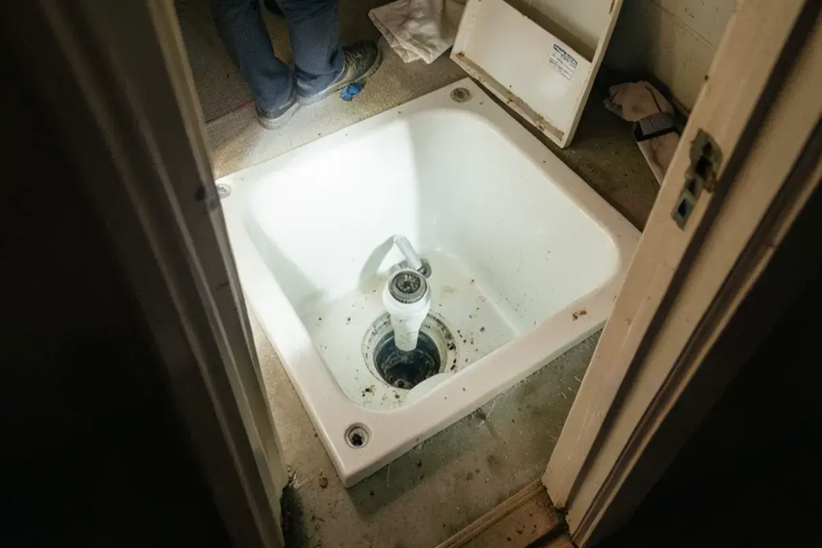 Tub waste-and-overflow fittings seen through an access panel in a closet wall behind a bathtub